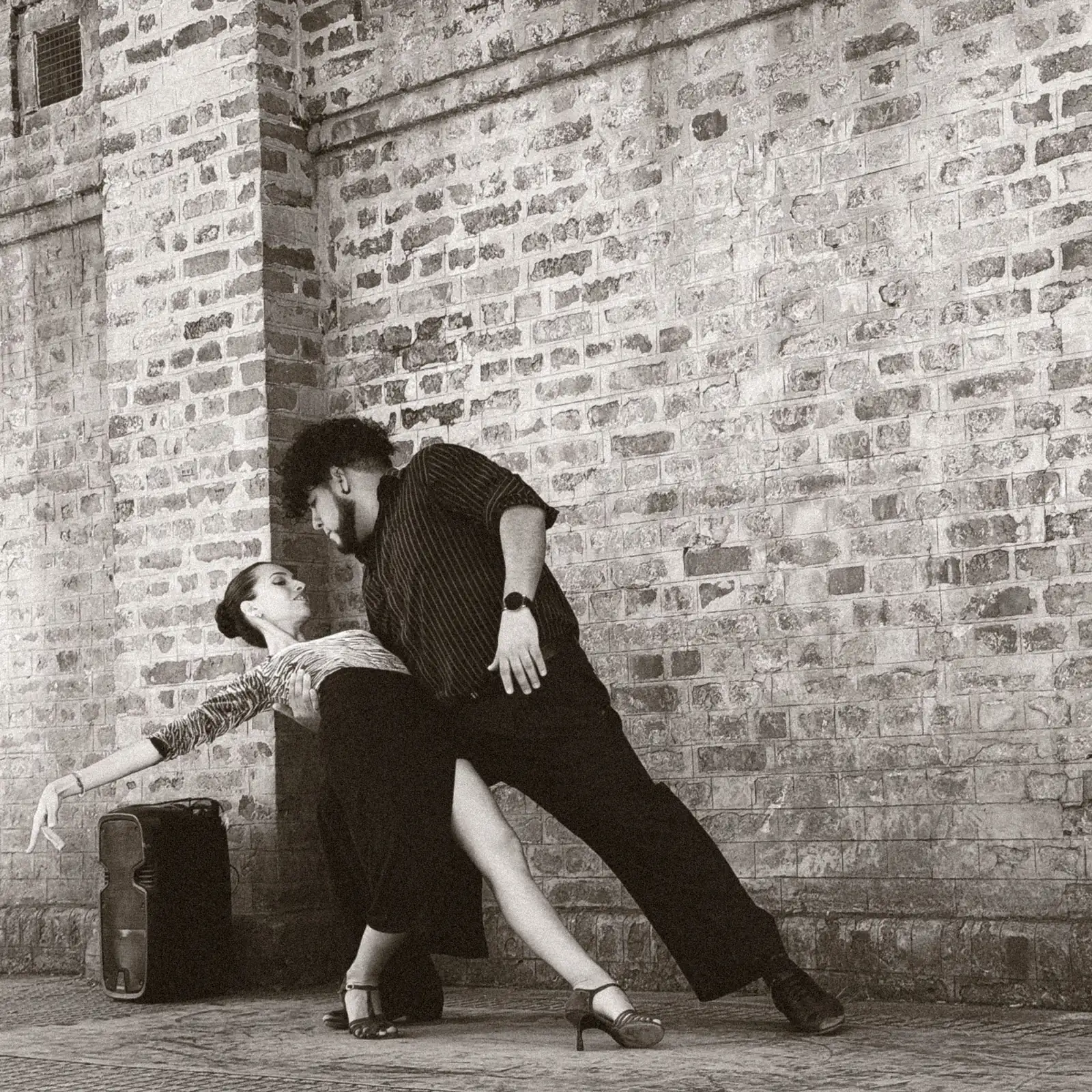 A tango couple mid-dip against a brick wall in Buenos Aires, sepia-toned