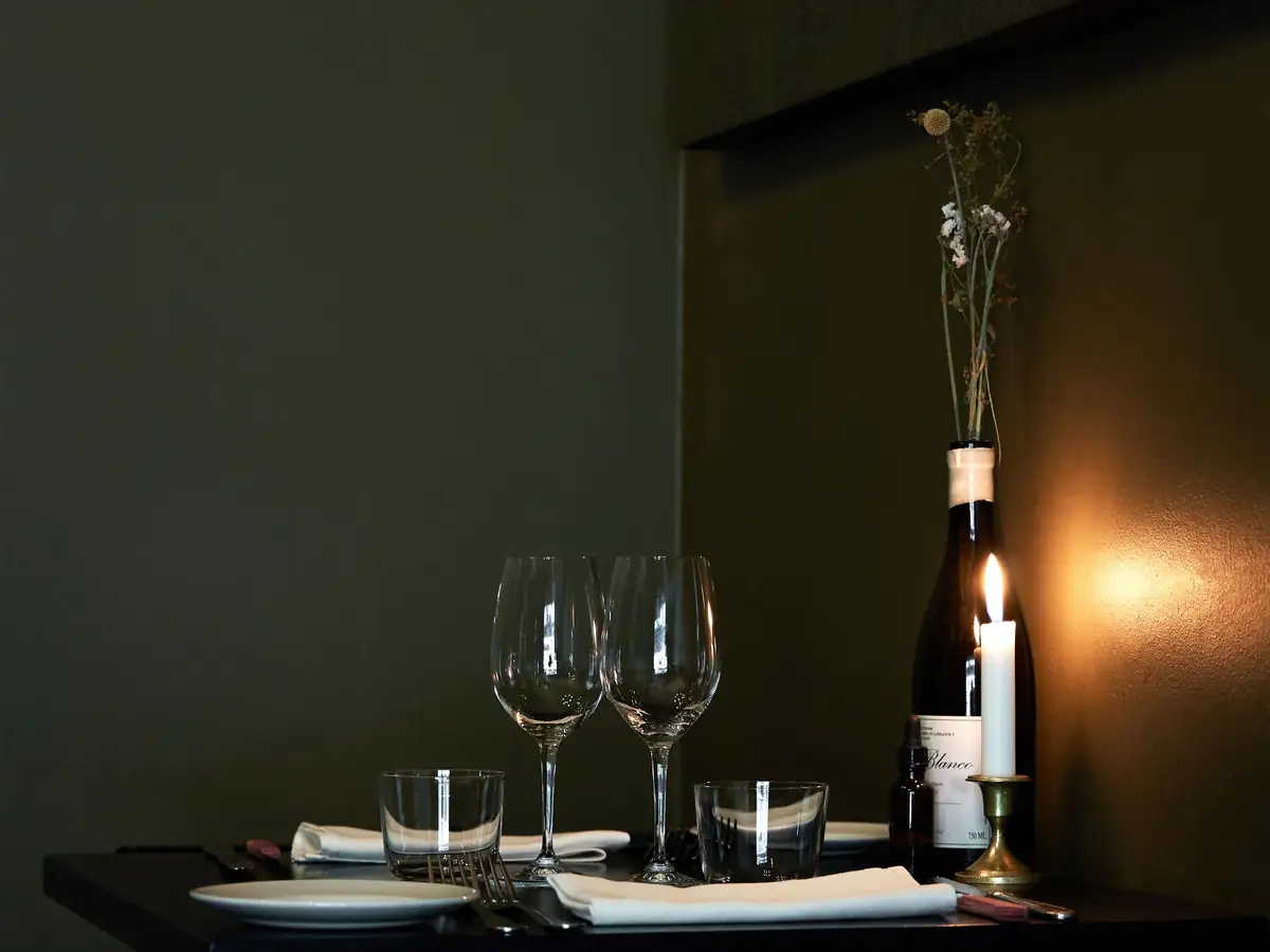 Two wine glasses and a candle on an elegant dark dinner table, representative of the evening's wine service